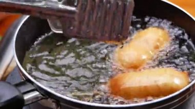 Hamur hamuruyla kaplanmış sosis şişleri ve mutfak ocağında sıcak yağda kızartılmış. Ev yapımı sosisli sandviç. yemek pişirme süreci.