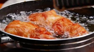 Tavuk budu kızartıyorum. Mutfak ocağında tavada sıcak yağda. Tavuk butlarını kızgın yağda döndürmek için mutfak maşası kullanan kadın eller. Sağlıksız Yemek.