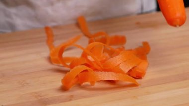 Kadın ellerinin yakın plan çekimleri kesme tahtasındaki soyucudan taze, sulu havucu soyuyorlar..