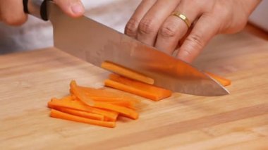 Kesme tahtasındaki bıçakla kadın ellerinin çiğ havuçları keserek sopa haline getirmesi..