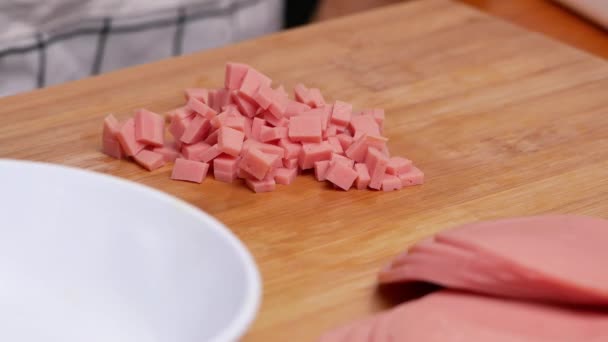 用切割板上的刀把生火腿肉片切成骰子的女手的特写 准备健康膳食的概念 — 图库视频影像