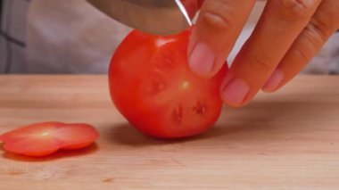 Dişi eller domatesleri tahta bir kesme tahtasıyla dilimler. Sağlıklı yemek hazırlama kavramı.