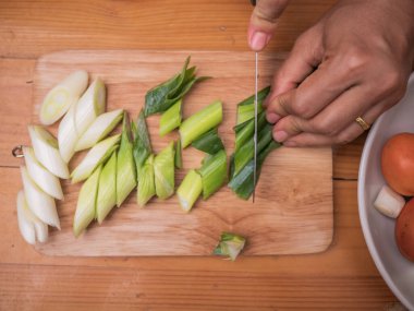 Japon Uzun Soğanı, Japon Scallion 'u ya da tahta kesme tahtasındaki Yeşil Soğan' ı kesmek için mutfak bıçağı kullanan bir kadın. Kadın mutfakta yemek hazırlıyor. Yemek pişirme konsepti.