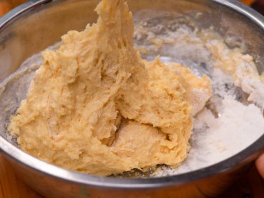 Un, taze süt ve tavuk yumurtalarını spatulayla karıştıran kadın eller ev yapımı mısırlı sosisler için hamuru hazırlar. Yemek pişirme süreci.