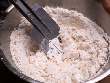 Un, taze süt ve tavuk yumurtalarını spatulayla karıştıran dişi eller ev yapımı çörekler için hamur hazırlar. Yemek pişirme süreci.