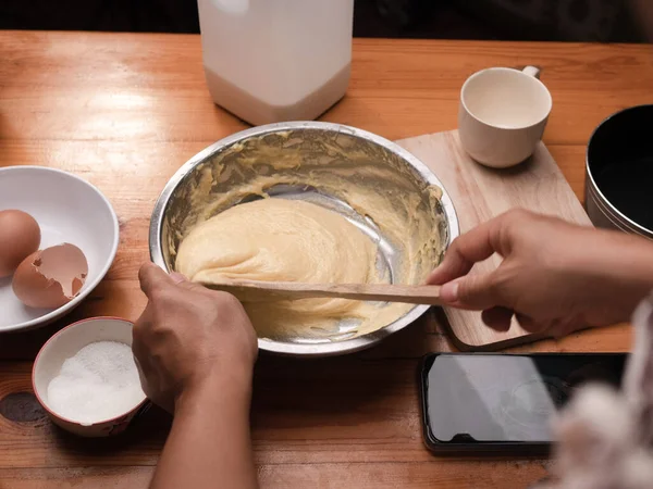 Un, taze süt ve tavuk yumurtalarını spatulayla karıştıran kadın eller ev yapımı mısırlı sosisler için hamuru hazırlar. Yemek pişirme süreci.