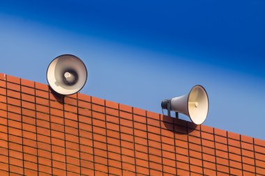 loudspeakers on builing and blue sky background clipart