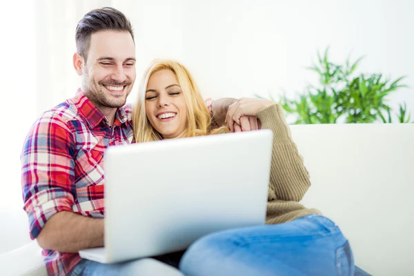 Молода пара переглядає Інтернет вдома, використовуючи ноутбук і посміхаючись — стокове фото