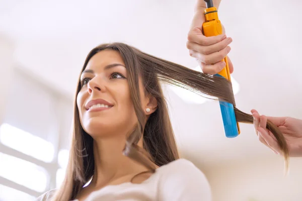 Giovane donna seduta mentre il parrucchiere si acconcia i capelli — Foto Stock