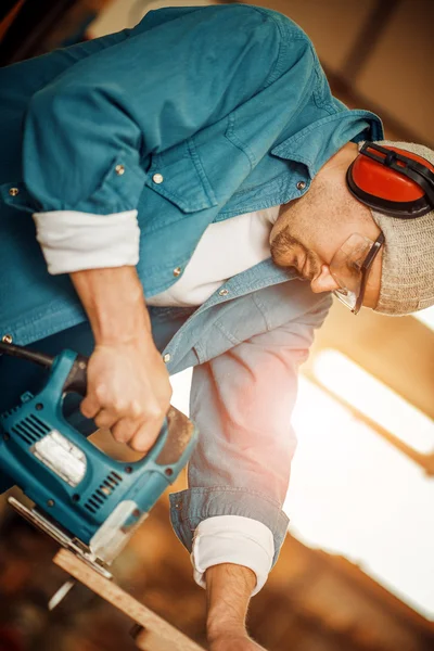 Muž řezání dřevěných planěk pomocí elektrické jig viděl — Stock fotografie