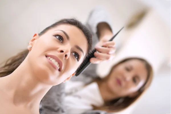 Giovane donna seduta mentre il parrucchiere si acconcia i capelli — Foto Stock