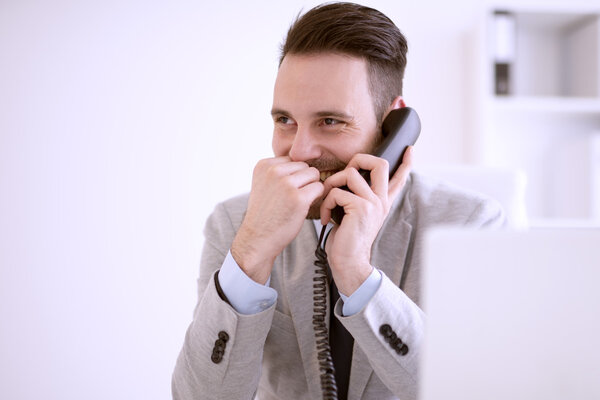 Businessman using laptop while talking on phone in the office