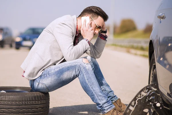 Ein junger Mann mit einem silberfarbenen Auto, das auf der Straße kaputt ging — Stockfoto