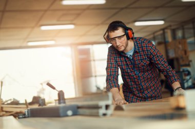 Marangoz atölyesinde testere kullanıyor.