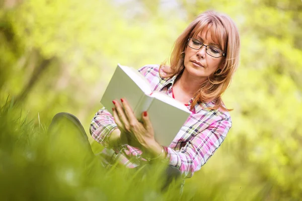 Atractiva mujer madura leyendo un libro en el parque —  Fotos de Stock