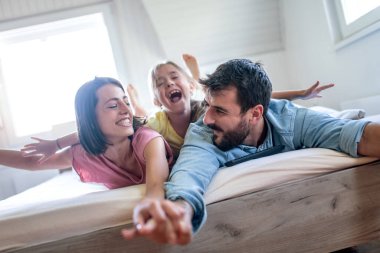 Birlikte televizyon seyreden gülümseyen genç bir aile. Boş vakitlerini yatak odasında geçiriyorlar..