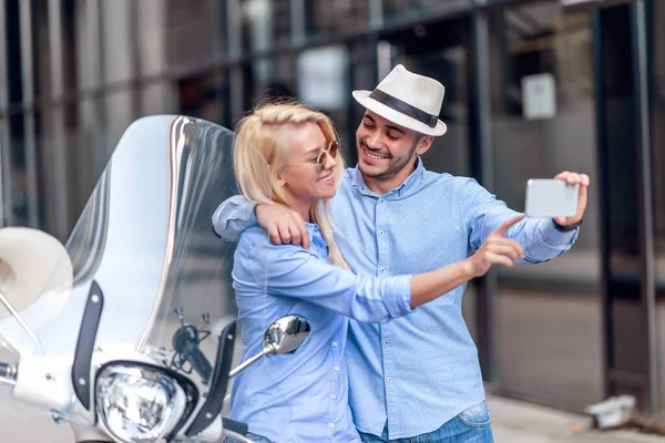 Happy couple on scooter taking selfie with phone in the city. Love, people and lifestyle concept.