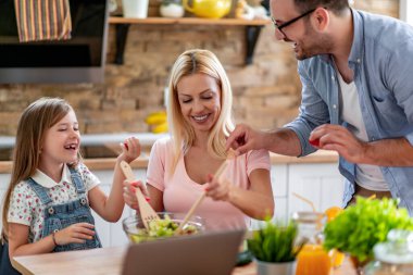 Genç bir aile mutfakta dizüstü bilgisayar kullanarak sağlıklı yemek tarifi arıyor..