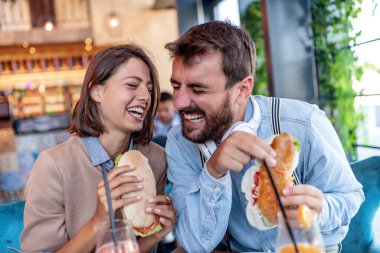 Genç ve neşeli çift meyve suyu içip kafede sandviç yiyorlar. İnsanlar, tarih, aşk ve yaşam tarzı konsepti.