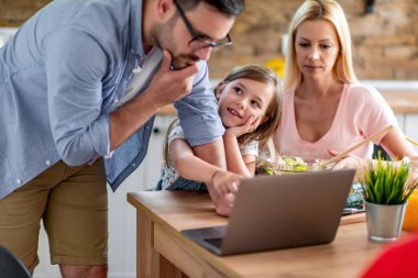 Genç bir aile mutfakta dizüstü bilgisayar kullanarak sağlıklı yemek tarifi arıyor..