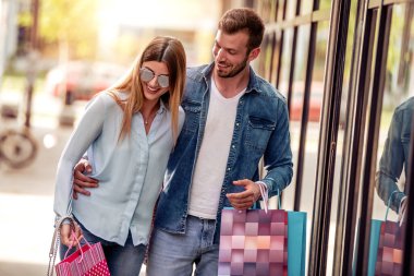 Birlikte alışveriş yapan genç bir çift, ellerinde alışveriş torbaları var..