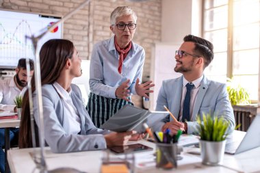 İş arkadaşları onu dinlerken kıdemli kadın gülümseyerek bir şey tartışıyor..