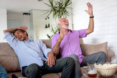 Küçük oğlu ve babası evde bira içerken futbol maçı izliyorlar. İnsanlar, keyif ve yaşam tarzı konsepti..
