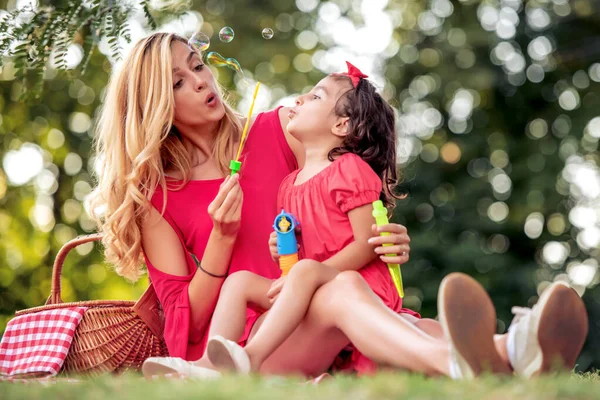 美しい母親と彼女の娘が公園でシャボン玉を吹いています — ストック写真