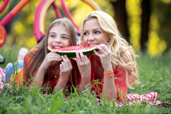Family time. Mother and daughter lying on the blanket  and eating watermelon in the park.