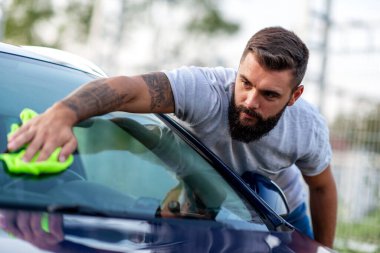 Arabasını dışarıda bir bezle temizleyen genç bir adamın portresi..