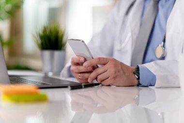 Doktorun ofisinde cep telefonu kullanmasına yakın çekim, doktor akıllı telefon üzerinde çalışıyor..