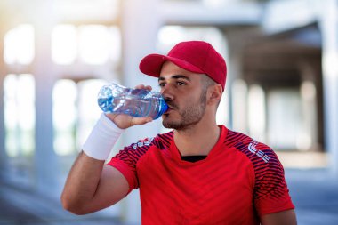 Sporcu, güneşli bir günde şehirde koştuktan sonra şişeden su içiyor..