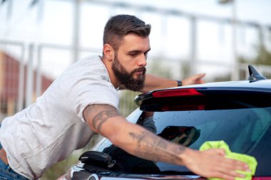 Genç adam arabasını kumaşla yıkıyor. Yıkama, yaşam tarzı ve insanlar konsepti.