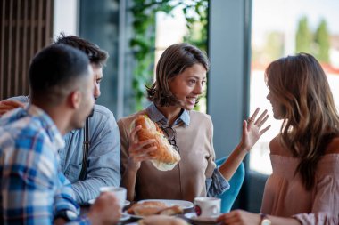 Bir grup insan bir kafede oturuyor, kahve içiyor ve hamur işi yiyor..