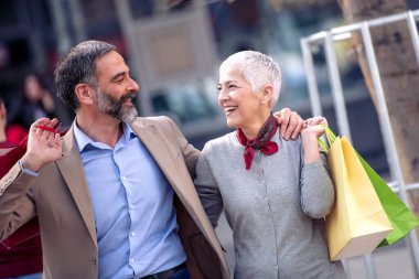 Alışveriş torbalarıyla yürüyen mutlu olgun çift..
