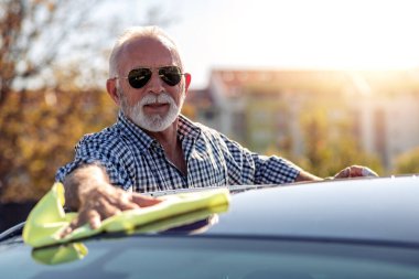 Dışarıda arabasını temizleyen kıdemli bir adam. Mikrofiberli bir adam arabanın cilasını siliyor..