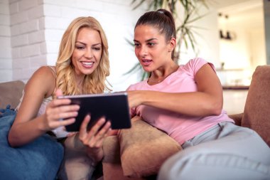 Evde tablet kullanan mutlu genç bayan arkadaşlar..