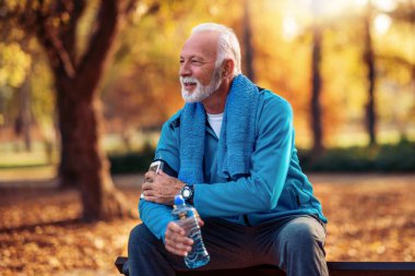 Kıdemli adam su içiyor ve dışarıda egzersiz yapıyor..