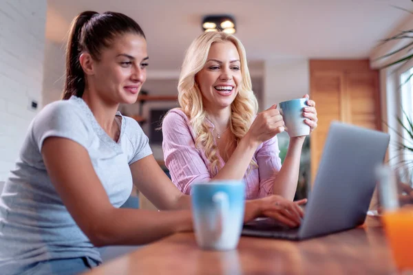Two beautiful women drinking coffee and using laptop.