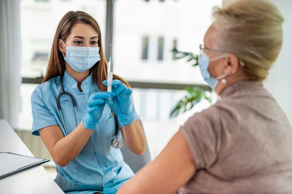 Female doctor giving a consultation to a senior patient.Doctor vaccinating senior patient in clinic.People,medicine and healthcare concept.