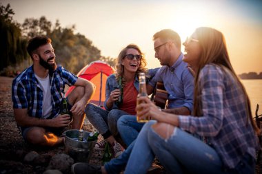 Bir grup genç arkadaş sahilde birlikte eğleniyor, kamp yaparken gitar çalıyorlar..