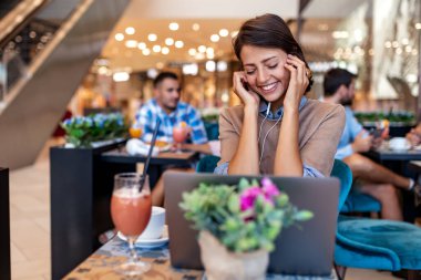 Kahve içen ve kafede dizüstü bilgisayara bakan çekici bir kadın..