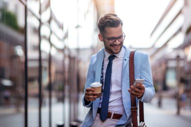 Genç işadamı mola verdi. Kahve içiyor ve dışarıda cep telefonu kullanıyor..