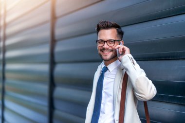 Ofise giderken elinde laptop çantasıyla gülümseyen bir işadamı. Telefonda. İş, insanlar ve yaşam tarzı konsepti..