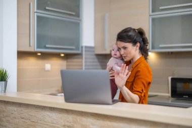 Çalışan anne konsepti. Evde bebeğiyle dizüstü bilgisayarda çalışan genç bir kadın. İş kadını iş ve anneliği dengeliyor..