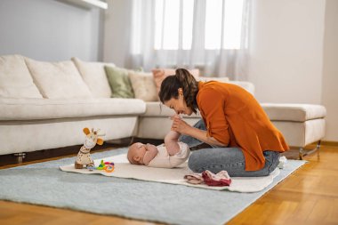 Gülümseyen genç anne evde bezini değiştirirken küçük bebekle eğleniyor. Anne yeni doğmuş bebeğin bezini değiştiriyor..