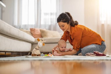 Gülümseyen genç anne evde bezini değiştirirken küçük bebekle eğleniyor. Anne yeni doğmuş bebeğin bezini değiştiriyor..