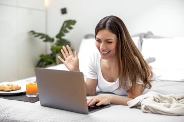 Mutlu kadın sabahları yatakta yatarken dizüstü bilgisayar kullanıyor..