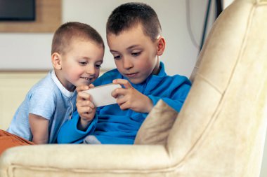 Evde birlikte akıllı telefondan oynayan çocukların portresi.