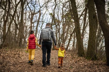 Aile, iki çocuklu bir baba ormanda yürüyüş yapıyor. Aile doğanın tadını çıkarıyor..